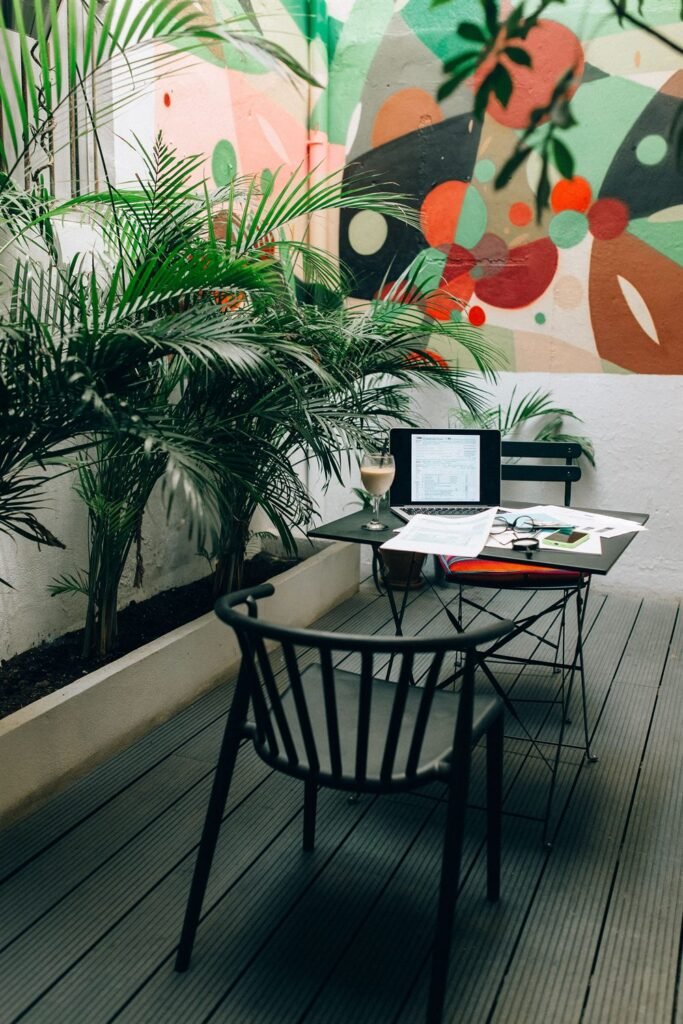 Small desk surrounded by tall potted palms in front of a colorful botanical mural